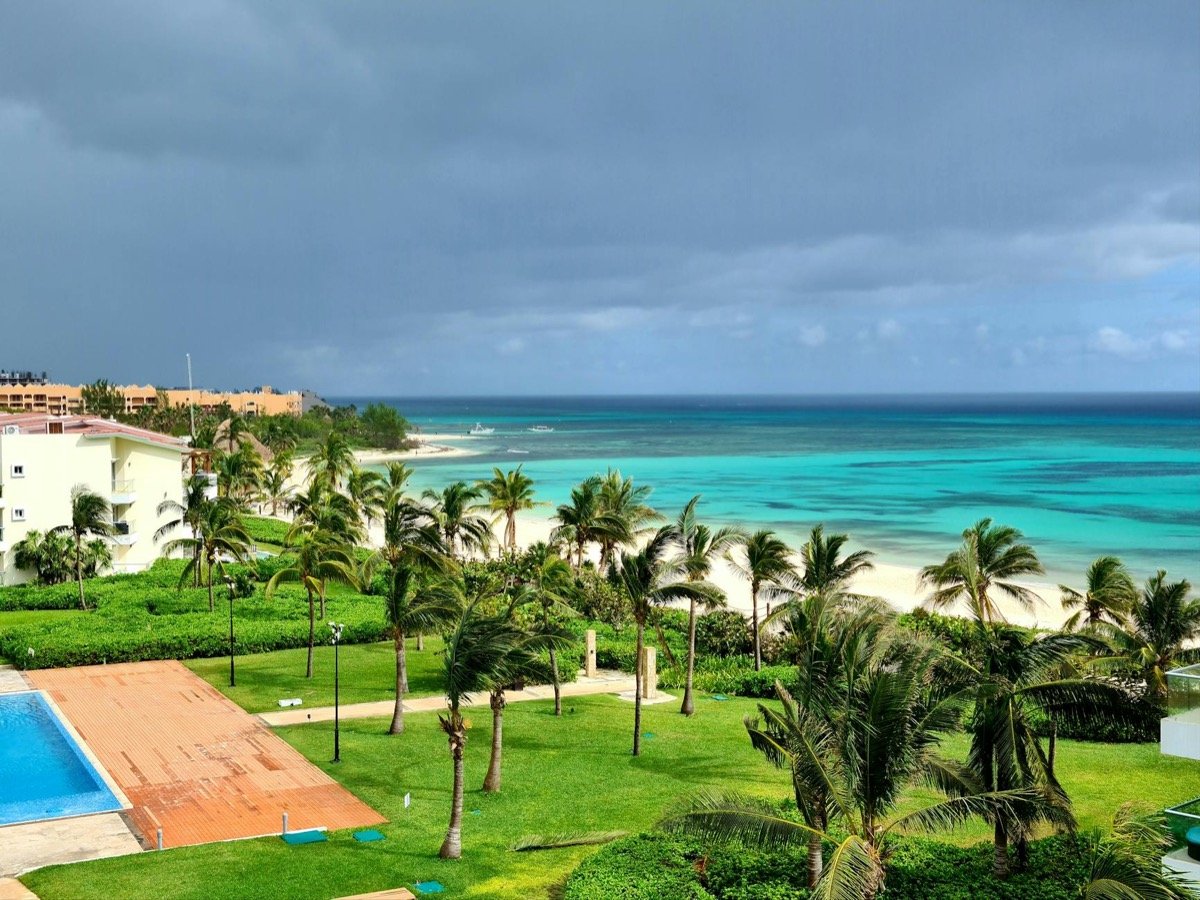 Luxury resort pool overlooking turquoise Caribbean water with palm trees and white sand beach below