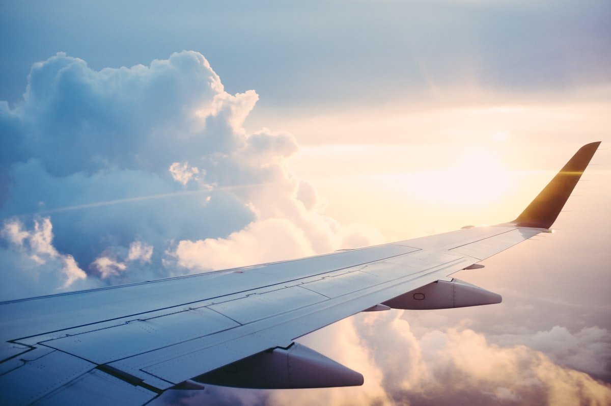 View from a private jet window above clouds at sunset, golden light across the wing